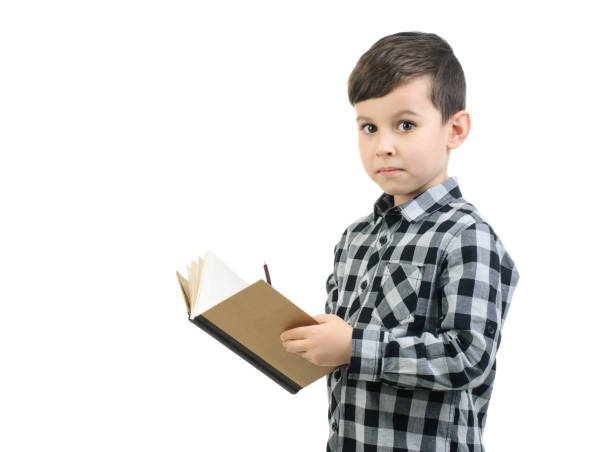 ragazzo di 6 anni con una camicia grigia scrive in un taccuino , scolaro sorpreso su sfondo bianco studio isolato. - 6 7 years foto e immagini stock