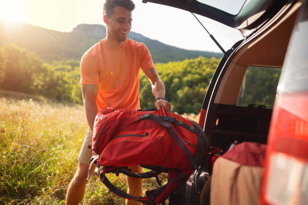 istock Happy young man putting backpack in the car trunk 1299179944