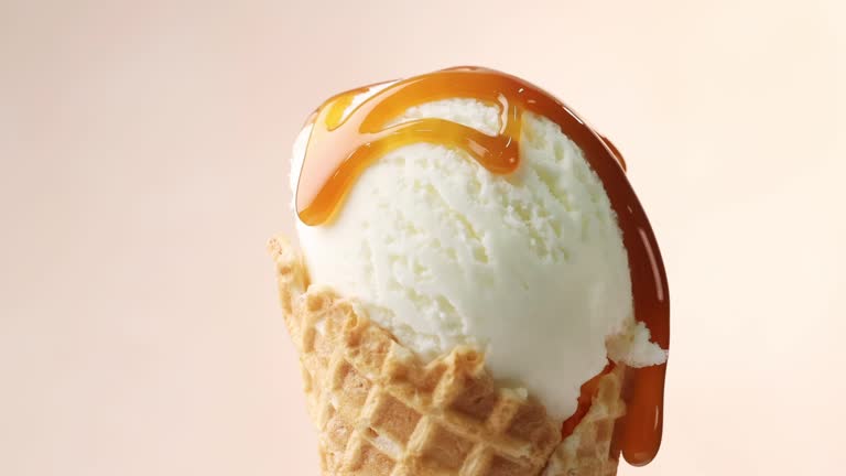 melted caramel sauce flowing on rotating vanilla ice cream in waffle scoop close up