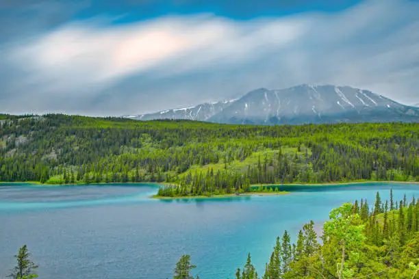 Beautiful landscape of Emerald Lake with turquoise water and misty snow capped mountains near Carcross, Yukon