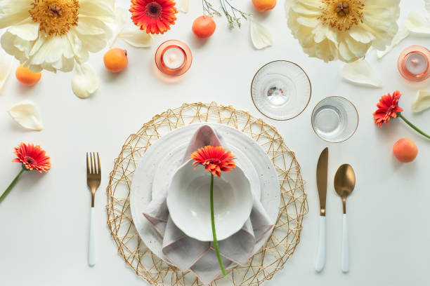 istock Effortless golden birthday dinner table decor. Summer flat lay. White dinner table, white and gold utensils, decorated with peony flowers, orange gerberas and apricots 1299182799