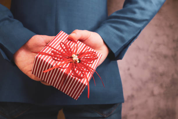 istock close up of man hands holding gift box behind his back 1299183504