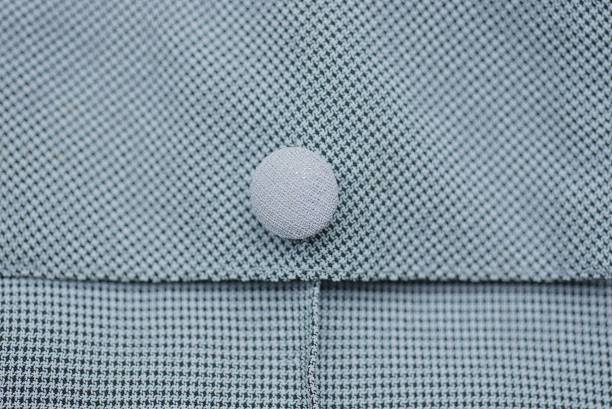 ein kleiner runder weißer knopf auf einem grauen kleidungsstück stoff - fashion rough jacket garment stock-fotos und bilder