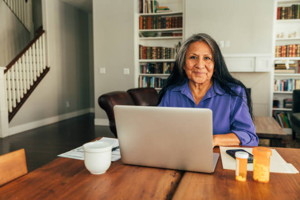 Senior Woman on Telemedicine Visit A senior aged woman sits at her kitchen table while paying medical bills, talking with her doctor, and updating medicine prescriptions. native american ethnicity stock pictures, royalty-free photos & images