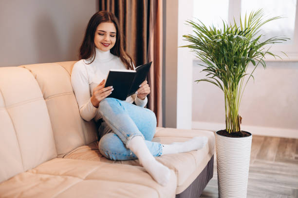istock Attractive and young woman is reading book / studying on sofa at home. 1299193035