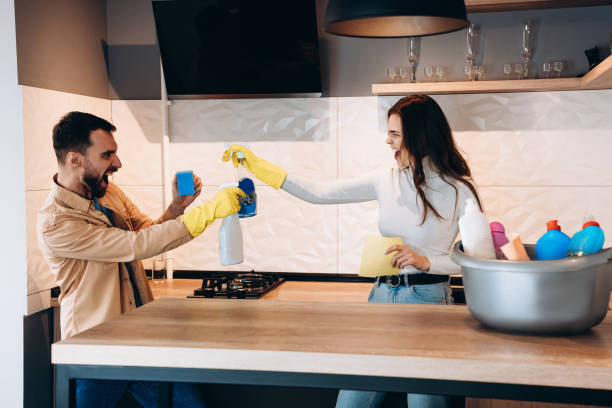istock Pretty couple having fun and pretending fight with cleaning tools in kitchen. 1299193092