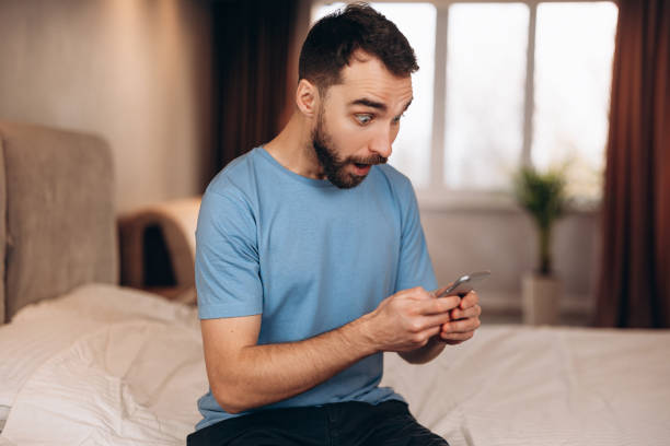 istock Young man with beard surprised shocked whilst received sending message on phone while sitting in bed. 1299193109