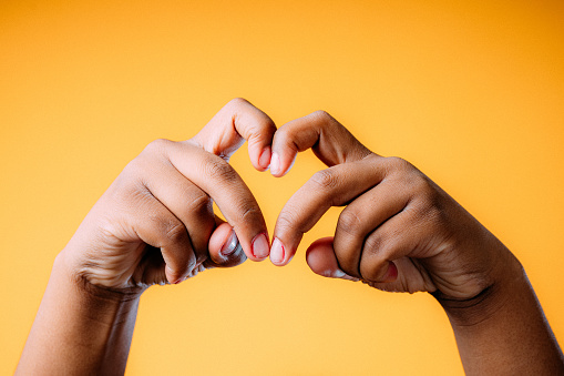 Retrato de estudio de una joven mujer afroamericana haciendo una forma de corazón única y divertida con sus dedos para mostrar amor, reconciliación o gratitud photo