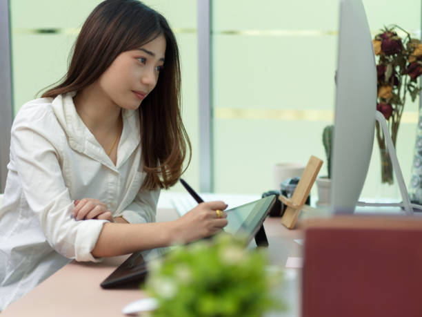istock Female office worker working on drawing tablet and computer in office room 1299198420
