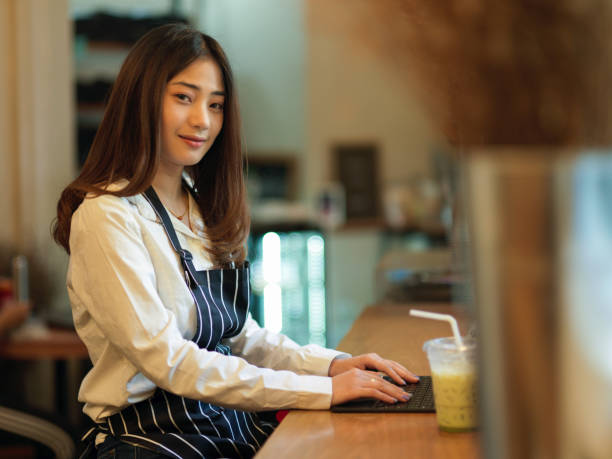 istock Female barista smiling to camera while using digital tablet on wooden bar in cafe 1299198444