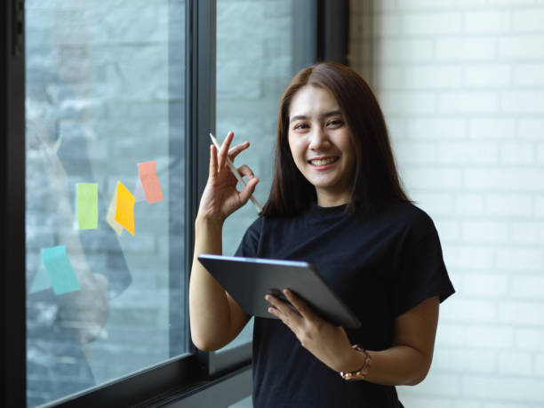 istock Businesswoman showing okey hand sign while working with tablet and idea on sticky note 1299198470
