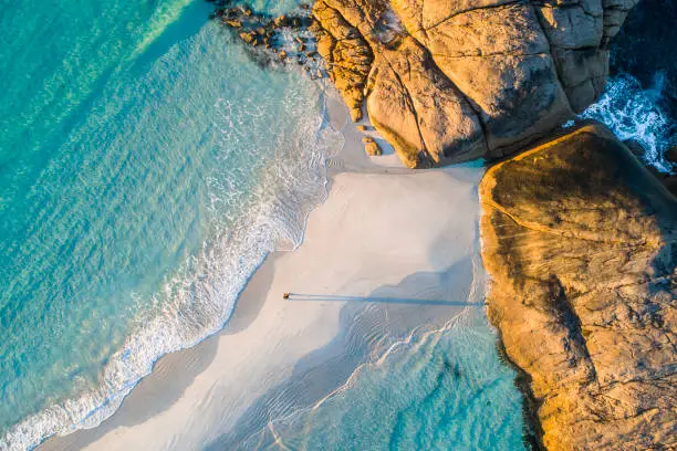 Coastline aerial photograph of aquamarine ocean and man walking along white sandbar beach in Australia