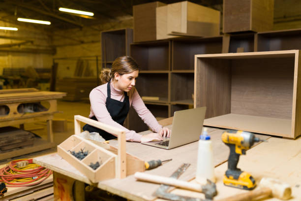 istock Beautiful carpenter sitting and using a laptop in her wood workshop 1299201404