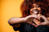 Studio Portrait of a Happy, Beautiful, Smiling Young African American Woman Making a Heart Shape with Her Hands to Show Love, Reconciliation, or Gratitude