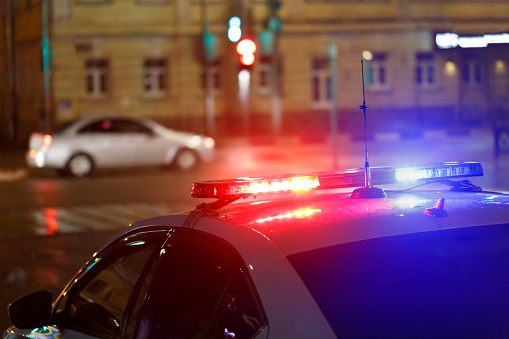 police car lights in street with civilian car in blurry background at night in european city