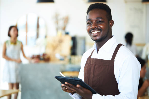 istock A black male waiter is standing and friendly smiling. 1299208795