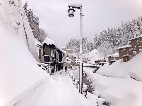 Beautiful Japanese winter scenery, small village with traditional houses, river, pine forest in snow on the hill, Ginzan onsen, nature of Yamagata, Japan