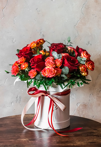 Beautiful bouquet of red roses in a box with ribbons on a wooden table. Beauty concept