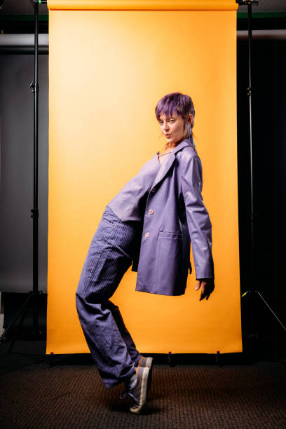 Artistic, Fun Studio Portrait of a Fashionable, Confident, Beautiful Person Standing in a Unique way on a Mustard-Yellow Background Studio Portrait of a Fashionable, Confident, Beautiful Non-Binary Genderqueer Person with a Short Purple Pixie Haircut on a Mustard-Yellow Background non binary gender photos stock pictures, royalty-free photos & images
