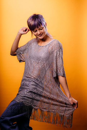 Studio Portrait of a Fashionable, Confident, Beautiful Non-Binary Genderqueer Person with a Short Purple Pixie Haircut on a Mustard-Yellow Background