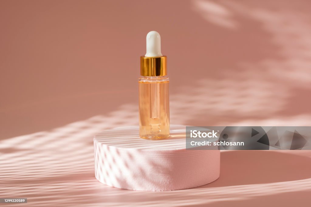 gold beauty serum in a pipette bottle on a pink podium with  shadows gold beauty serum in a pipette bottle on a pink podium with  shadows on a coral pink background Hyaluronan Stock Photo