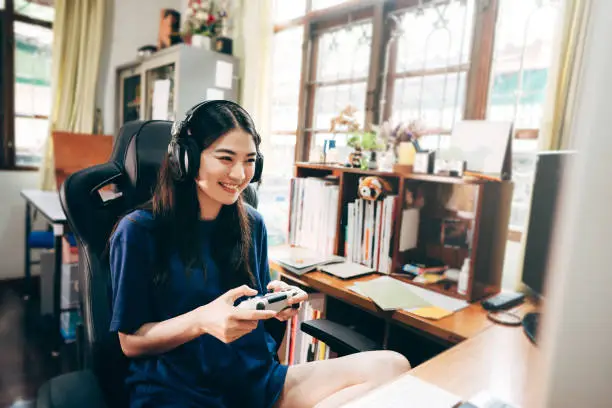 Young adult asian woman hand holding a joy controller wear headset and play game. People relax and entertainment lifestyle at home concept