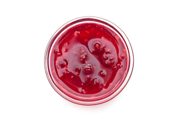 Photo of Raspberry jam in glass bowl, liquid jam isolated on white, top view, lay out with space for text