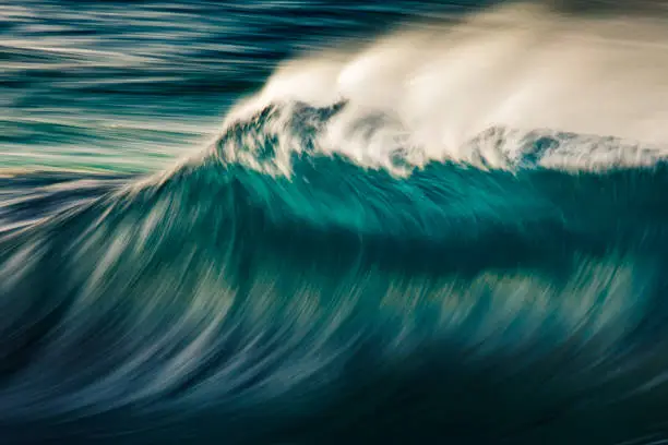 Photo of Cresting wave breaking with wind spray in the morning light