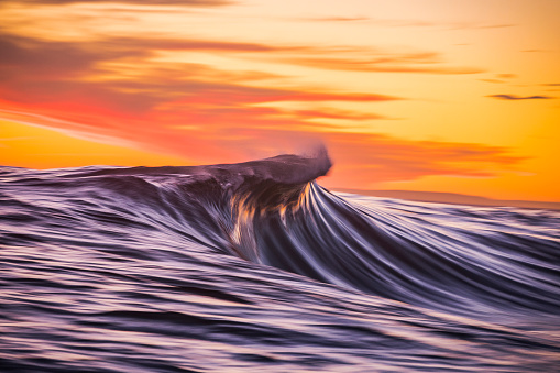 Cresting wave breaking in brilliant orange and golden morning light