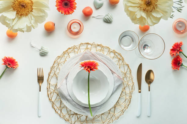 istock Effortless golden birthday dinner table decor. Summer flat lay. White dinner table, white and gold utensils, decorated with peony flowers, orange gerberas and apricots 1299224567
