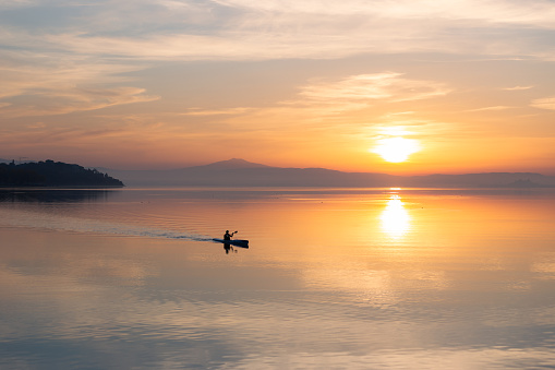 Beautiful sunset at Trasimeno lake with a man on a canoe above perfectly still water.