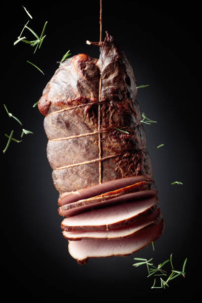 istock Sliced smoked ham with rosemary on a black background. 1299230260