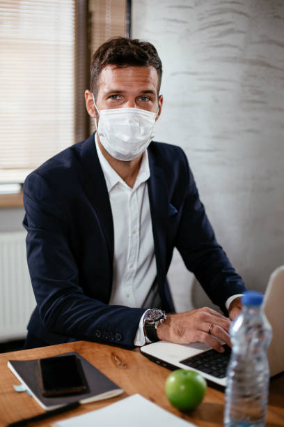 istock Young businessman with a mask working in his office on laptop. 1299230509