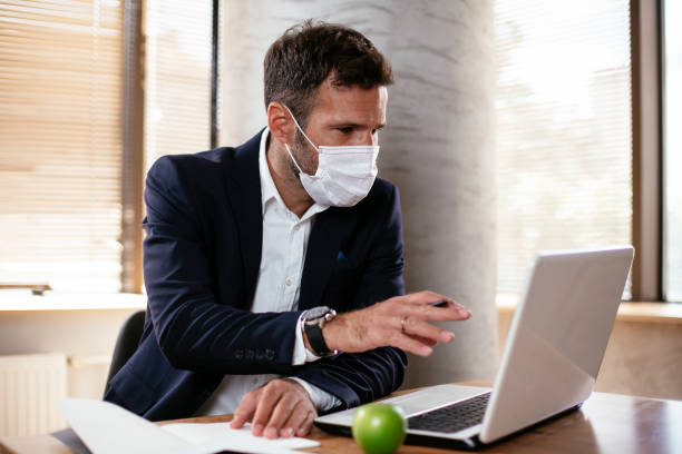 istock Young businessman with a mask working in his office on laptop. 1299230596