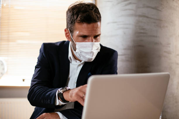 istock Young businessman with a mask working in his office on laptop. 1299230600