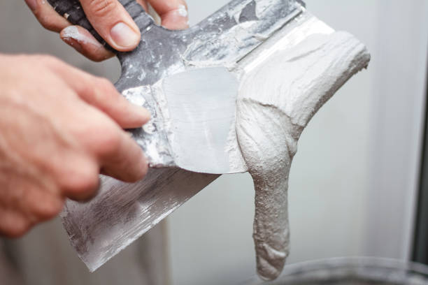 istock Man's hand removes excess plaster from the spatuia. 1299232400