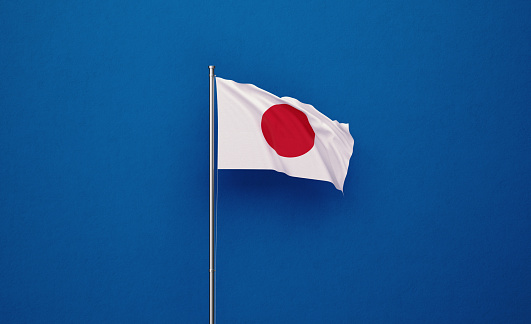 Japanese flag attached to a flagpole waving over navy blue background. Great use for Japanese politics and Japanese culture related concepts.