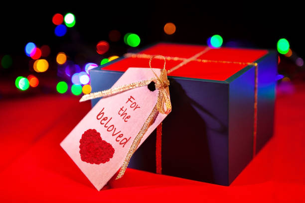 istock Gift box label with text - for the beloved, red background with colorful lights from the back. 1299234028