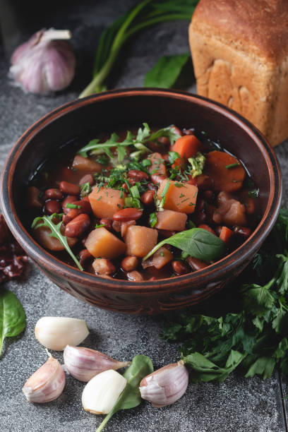 istock Bean soup with herbs in a clay bowl with fresh rye bread and garlic on a slate table on a dark background 1299235193