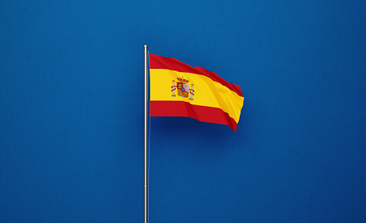 Spanish flag attached to a flagpole waving over navy blue background. Great use for Spanish politics and Spanish culture related concepts.