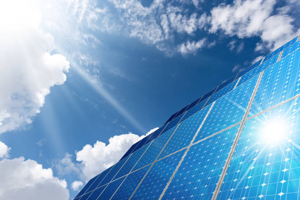 istock Large Group of Solar Panels on Blue Sky with Clouds and Sun Rays 1299238138