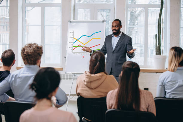istock Male speaker giving presentation in hall at workshop. Audience or conference hall. Rear view of unrecognized participants. 1299240352
