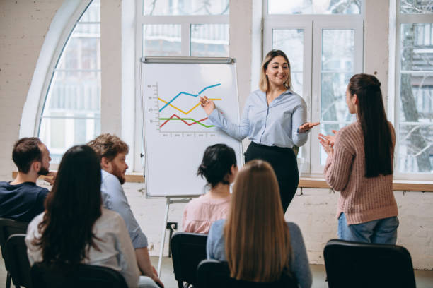 istock Female speaker giving presentation in hall at workshop. Audience or conference hall. Rear view of unrecognized participants. 1299240398
