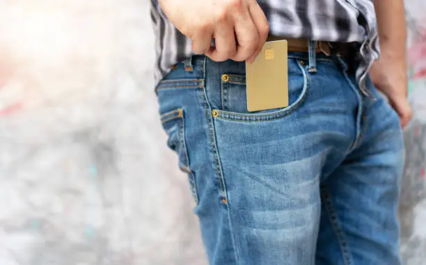 Photo of Hands of young man pick up empty gold generic credit card out of jeans pocket. Concept of losing money, business and finance.