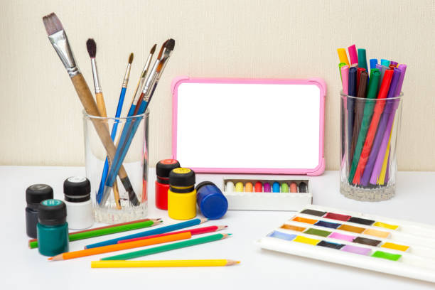 istock Children's digital tablet with a blank screen on a white table with multicolor drawing supplies. 1299243007