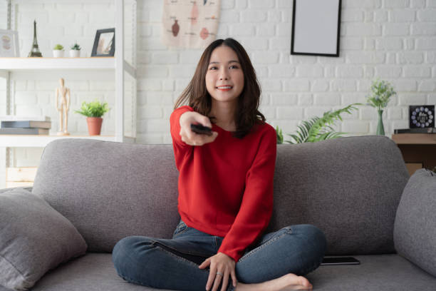 woman sitting on a sofa watching tv in the home. - remote television movie box imagens e fotografias de stock