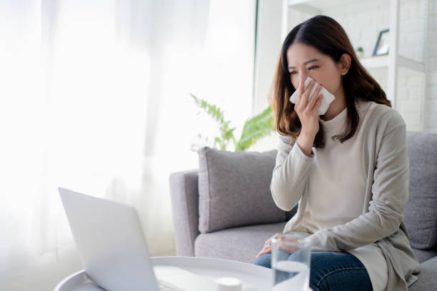 istock Young Asian women cough and sneeze while working at home. She feels sick. 1299244270