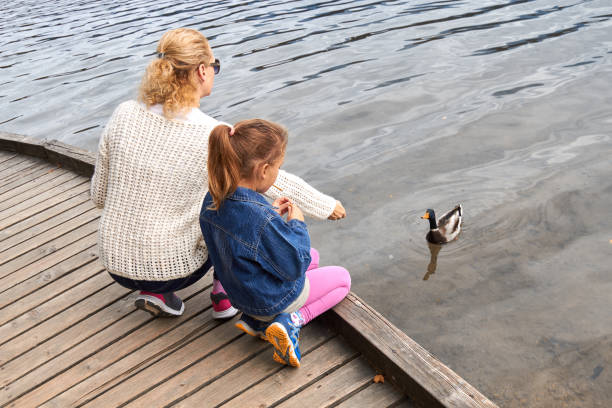 istock Mother and daughter feeding duck on a lake. 1299244918