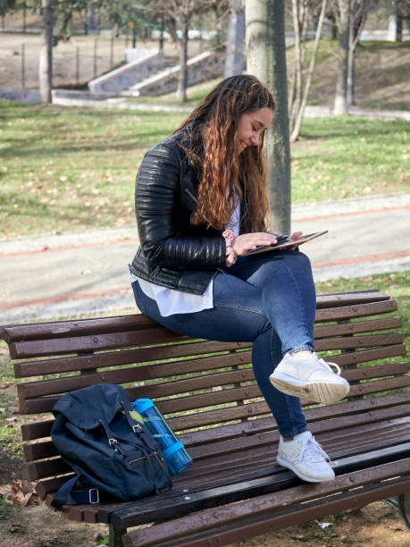 istock Young caucasian female using her tablet while sitting on a wooden bench in the park 1299247759