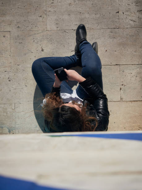 An overhead shot of a young female using her smartphone while sitting on the ground